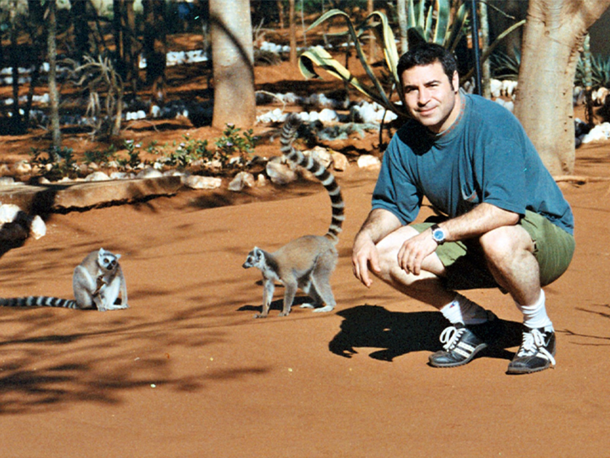 Peter in a blue T-shirt in green shorts, kneels beside two lemurs.