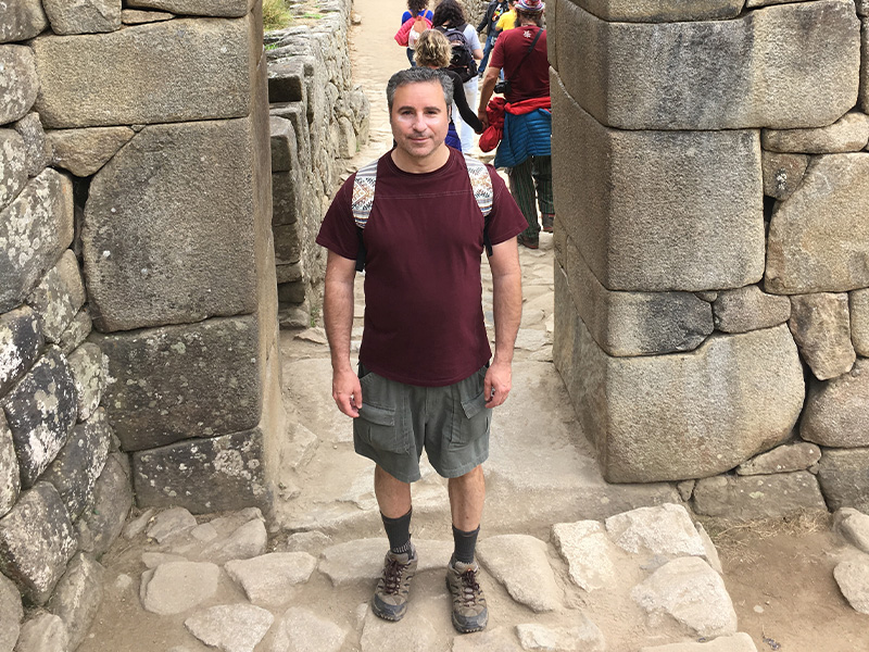 Peter Alexander stands wearing a backpack and khaki shorts in a doorway at Monte Picchu, Peru.